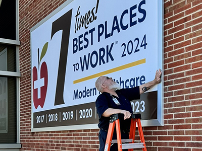 Image of JRMC Facilities Supervisor Joey Cotton installs Best Places to Work banner.